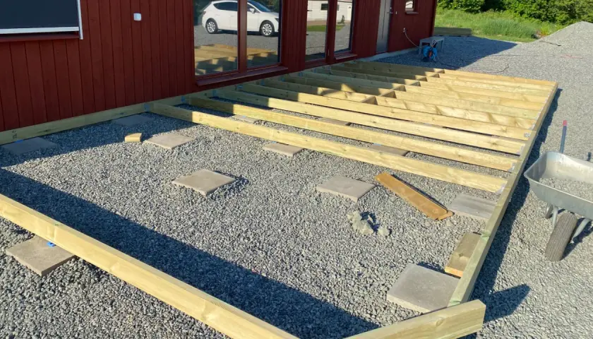 Grundarbete för att bygga altan på plattor. Träreglar läggs ut på grus och stenplattor, redo för altandäck.