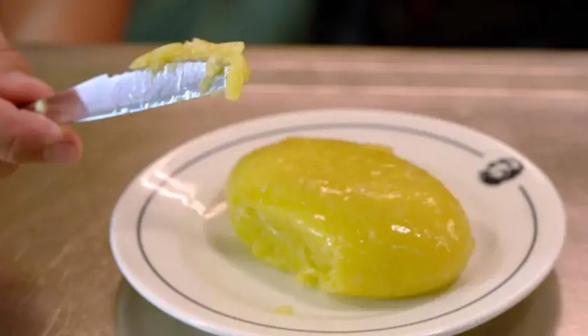 Un cuchillo recoge una porción de cremoso alioli casero, listo para untar sobre un plato blanco.