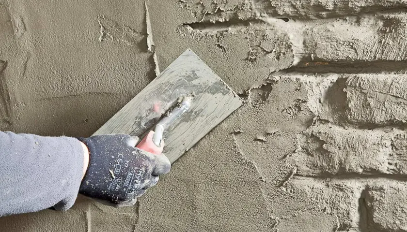 Hand mit Handschuh glättet Mörtel auf Bruchsteinmauer. Abdichten des Kellers mit Putz.