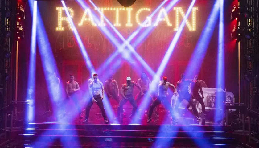 Mężczyźni tańczą na scenie w świetle niebieskich reflektorów, pod neonowym napisem "RATTIGAN". To scena z filmu Magic Mike 1.