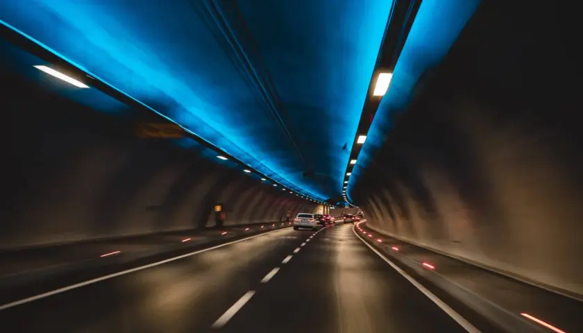 Jadące samochody w tunelu drogowym z niebieskim oświetleniem sufitowym.