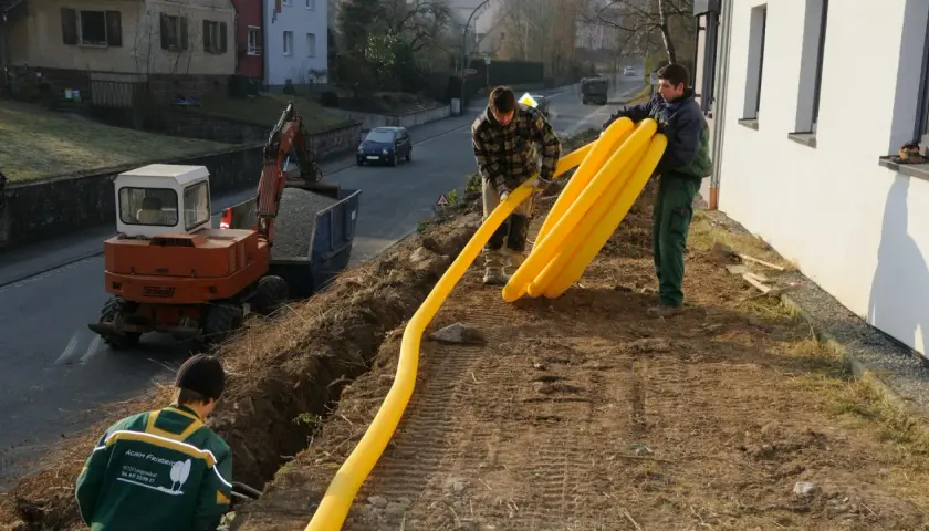 Arbeiter verlegen gelbe Rohre für die Drainage am Keller. Ein Bagger steht bereit.