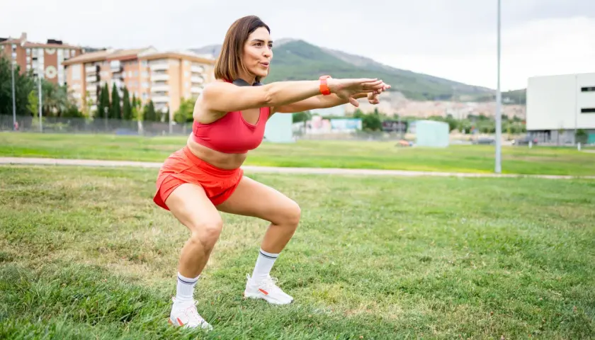 Kobieta w czerwonym stroju sportowym wykonuje przysiady na trawie. To część jej treningu, która pomaga jej odpowiedzieć na pytanie "kim jestem?".