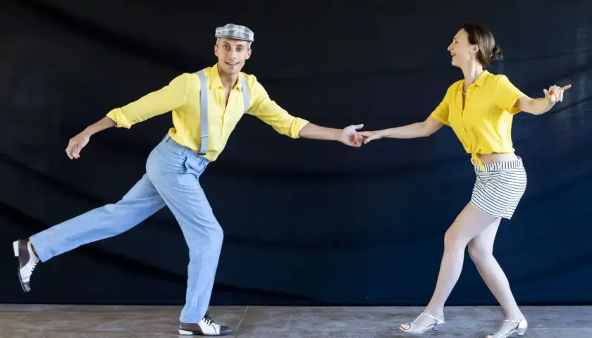 Coppia in abiti vintage che esegue un energico lindy hop ballo, con lui in giallo e bretelle, lei in giallo e gonna a righe.