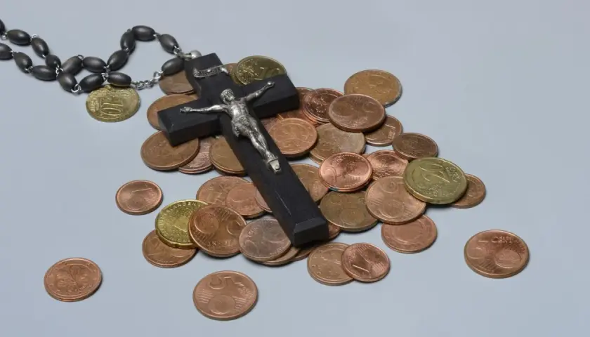 Holzkreuz mit Korpus, Rosenkranz und Münzen. Ein Symbol für das Kirchgeld in Bayern.