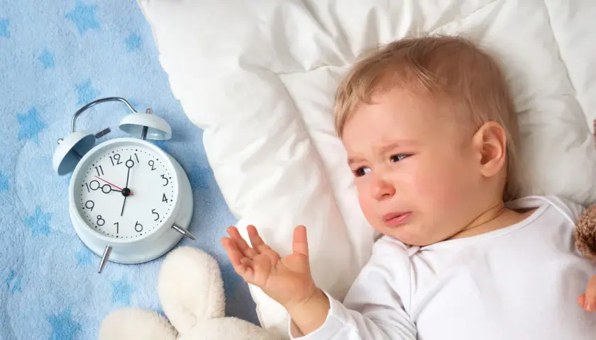 Płacz 1,5 rocznego dziecka, które nie chce spać. Obok budzik i pluszaki.