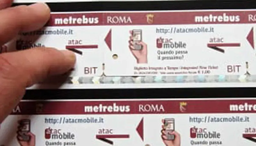 Dita sfiorano un biglietto metro Roma da 2 euro, con logo Atac e indicazioni per l'acquisto online.