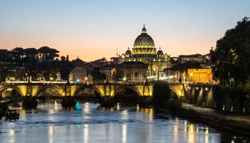 Ponte Sant'Angelo illuminato al tramonto, con Castel Sant'Angelo e la cupola di San Pietro. Un'idea su cosa fare il pomeriggio a Roma.