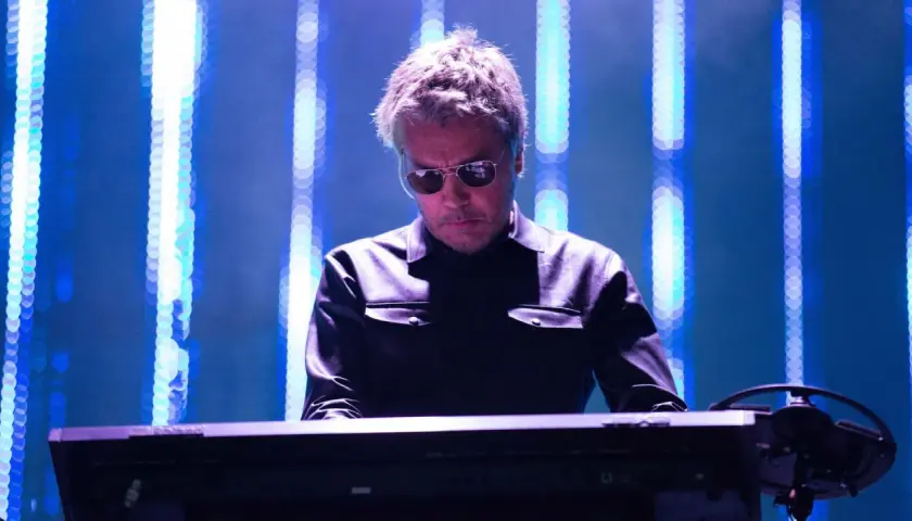 Jean Michel Jarre w Polsce, w okularach przeciwsłonecznych, gra na syntezatorze na tle niebieskich świateł.