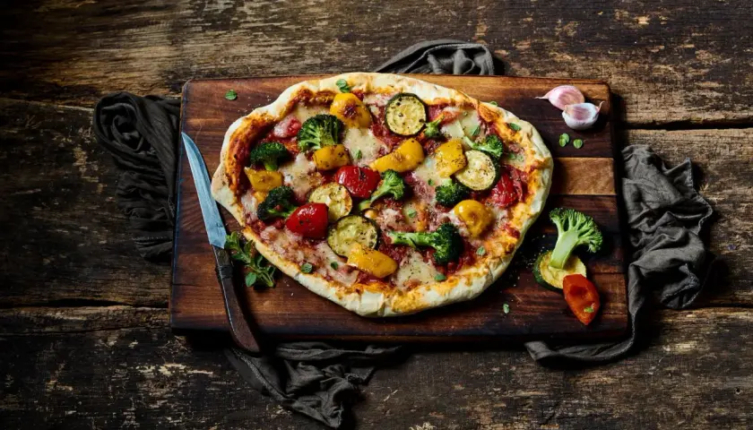 Eine köstliche vegane Pizza mit buntem Gemüse-Belag: Brokkoli, Zucchini, Paprika und Tomaten.