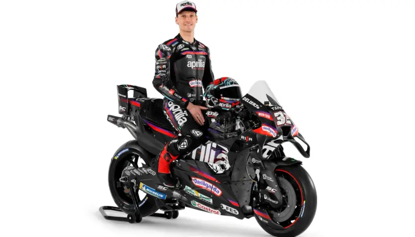 Piloto de Aprilia MotoGP posa junto a su moto de carreras negra y roja, listo para la acción.