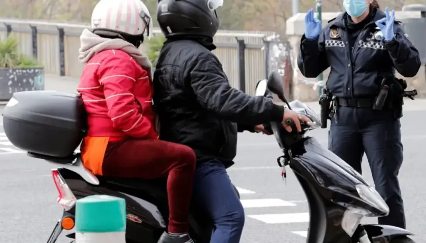 Agente de policía detiene a pareja en moto. Podrían recibir una multa por ir sin casco.