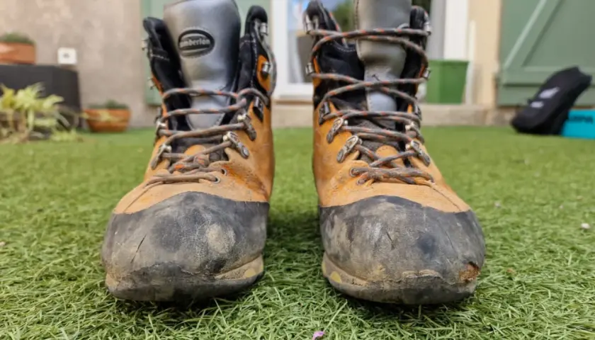 Bottes de randonnée usées, prêtes à être ressemelées. Elles ont vu du terrain et méritent une seconde vie.