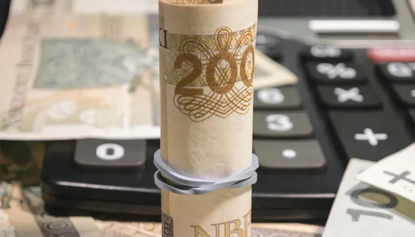 Zrolowany banknot 200 zł na kalkulatorze, obok inne nominały. Analiza millenium kurs akcji.
