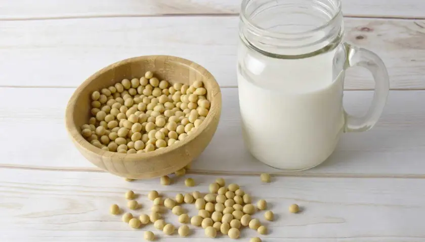 Bol en bois rempli de graines de soja, à côté d'un verre de lait de soja. La lécithine de soja est un ingrédient clé.