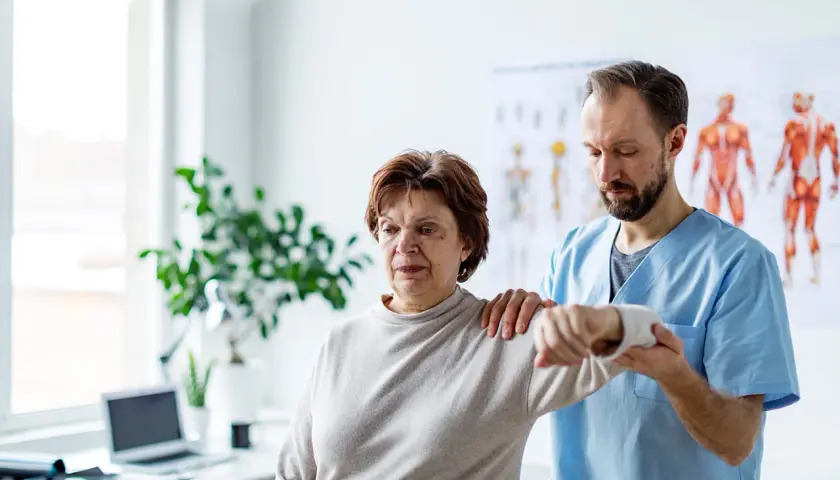 Physiotherapeut hilft einer Frau mit einer schmerzenden, verklemmten Schulter bei der Bewegung.