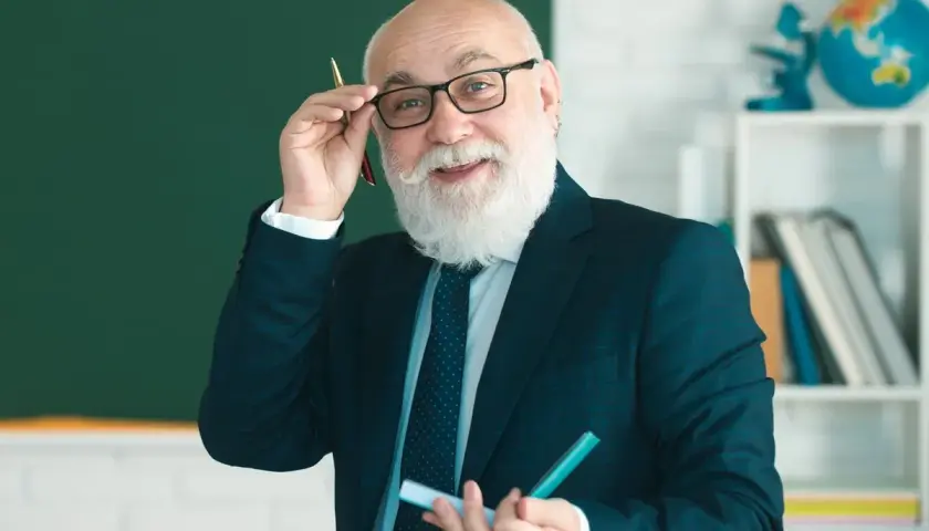 Uśmiechnięty starszy nauczyciel w okularach i garniturze trzyma długopis i marker.