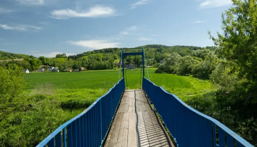 Mostek na szlaku trzech pogórzy prowadzi przez zielone pola i lasy.