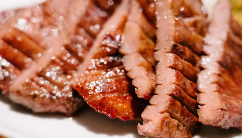 Tranches de langue de bœuf grillée, tendres et juteuses, servies sur une assiette blanche.