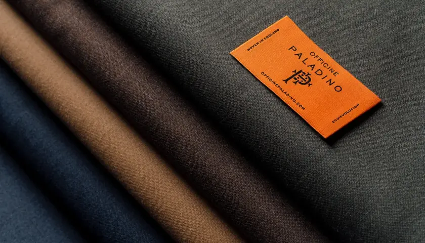 A selection of different types of wool fabric in shades of blue, brown, and grey, with an orange tag from Officine Paladino.