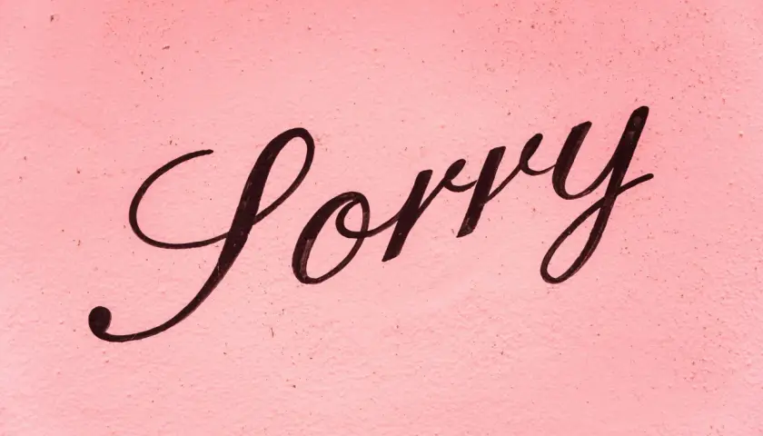 Napis "Sorry" czarną, ozdobną czcionką na różowym, chropowatym tle.