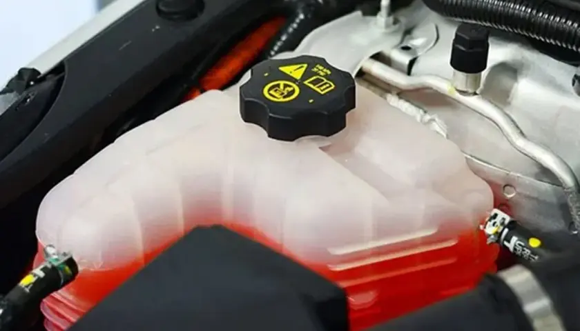 Depósito de refrigerante de coche con líquido rojo. La tapa negra tiene símbolos de advertencia. Se puede echar agua normal al coche si es necesario.