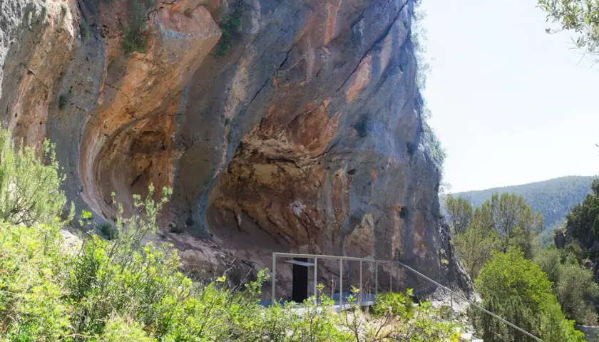 La cueva de la araña, una entrada moderna a una formación rocosa natural, se asoma entre la vegetación.