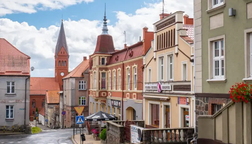 Ulica w gminie Skarszewy z kościołem w tle i kolorowymi kamienicami.