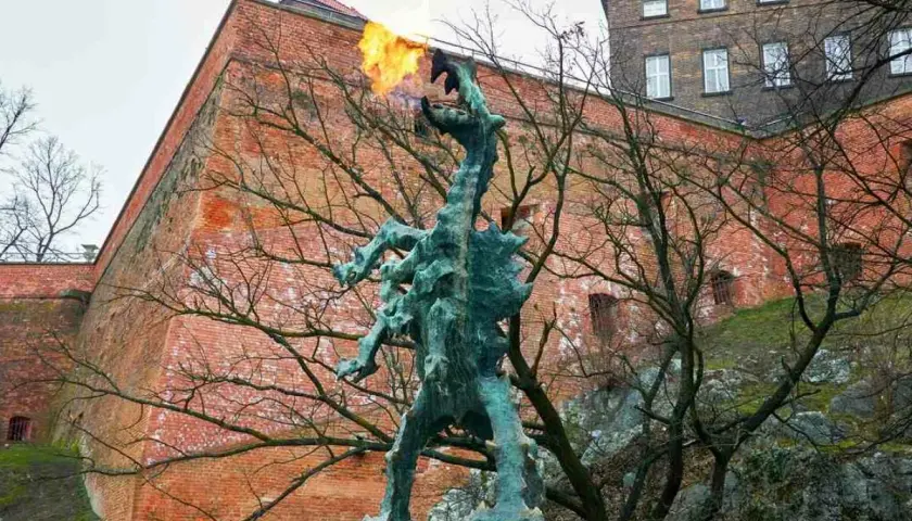 Smok Wawelski ziejący ogniem, pomnik nawiązujący do legendy, na tle ceglanych murów Wawelu.