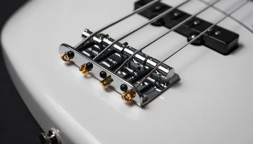 Błyszczące, chromowane struny do gitary basowej 4 strunowej na białym korpusie instrumentu.