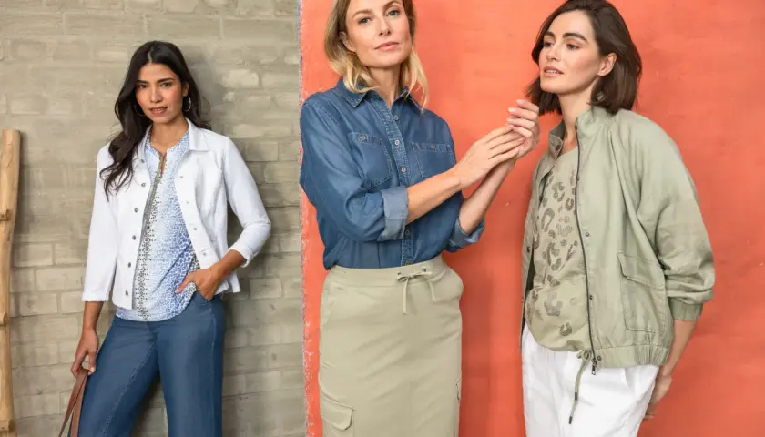 Trzy kobiety w casualowych stylizacjach. Jedna w białej marynarce i dżinsach, druga w dżinsowej koszuli i beżowej spódnicy, trzecia w zielonej kurtce i białych spodniach. Idealny stroj na poprawiny.