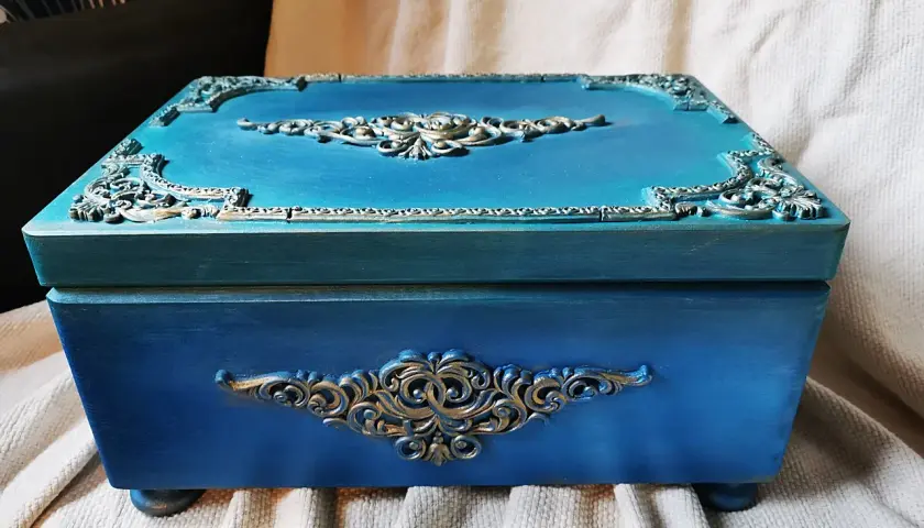 Elegancka, turkusowa skrzynia na skarby z ozdobnymi, złotymi ornamentami. Idealna do przechowywania cennych drobiazgów.