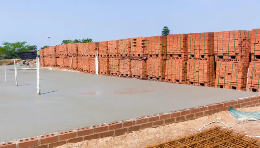 Frisch gegossener **fundamentbeton c25/30** wartet auf die Ziegelstapel, die daneben lagern.