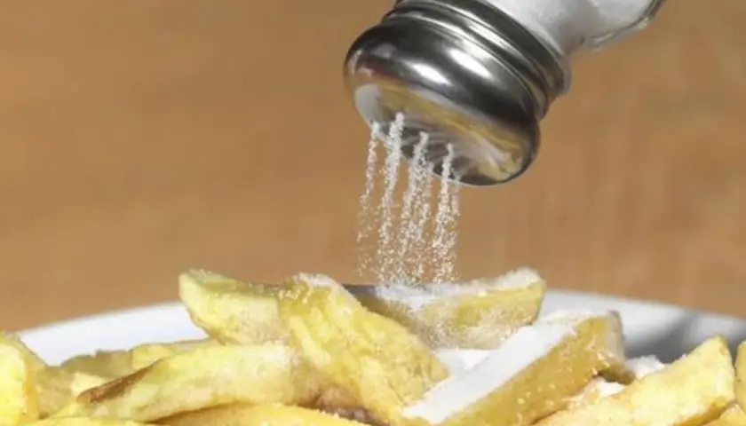 Salzstreuer rieselt Salz auf Pommes. Zu viel Salz essen kann zu Problemen führen.
