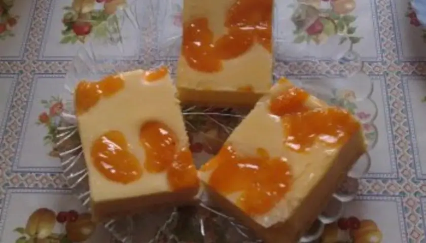 Drei Stücke faule weiber kuchen mit Mandarinen auf einem Tisch mit Blumenmuster.