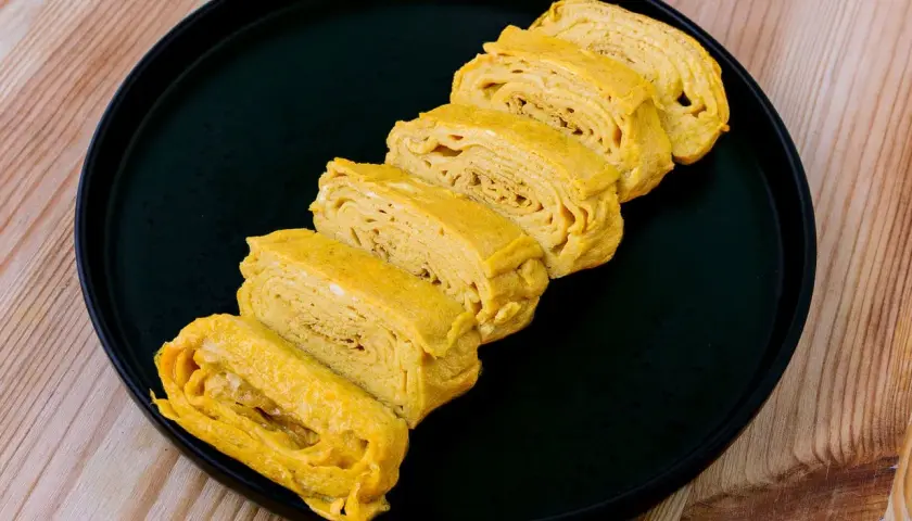 Tranches d'oeuf tamago, un délice japonais, disposées sur une assiette noire.