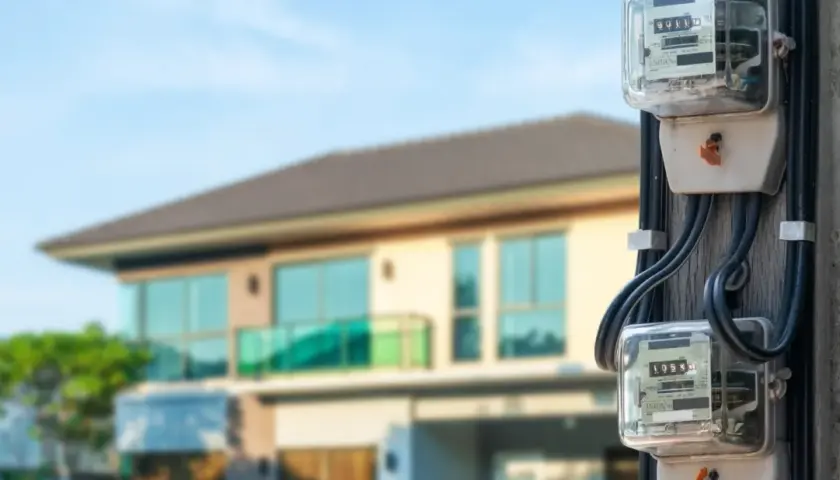 Medidores de luz, sensores eléctricos, en un poste frente a una casa moderna.