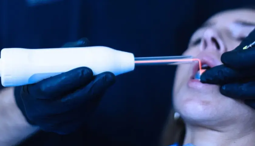 Trattamento laser per come rinforzare le gengive. Un professionista usa uno strumento con luce rossa su una bocca.