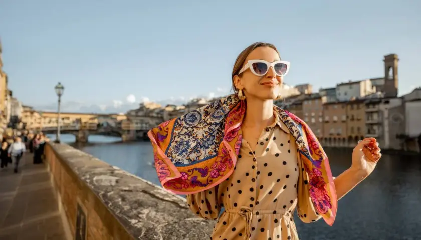 Kobieta w okularach i wzorzystym szalu na tle florenckiego mostu. Popielniczka po włosku, czyli piękny widok.