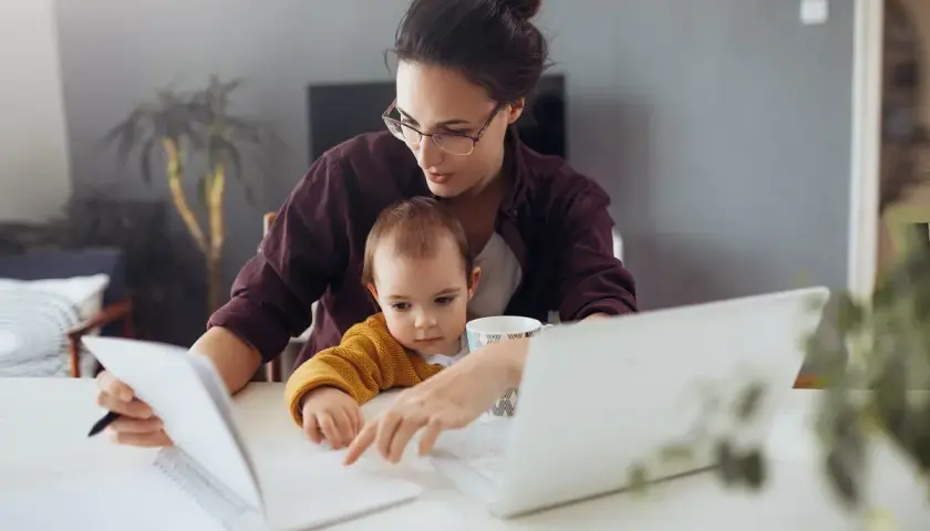 Mama z dzieckiem przy biurku, pracująca zdalnie. Kosiniakowe dla kogo? Dla wszystkich rodziców łączących pracę z opieką nad dzieckiem.