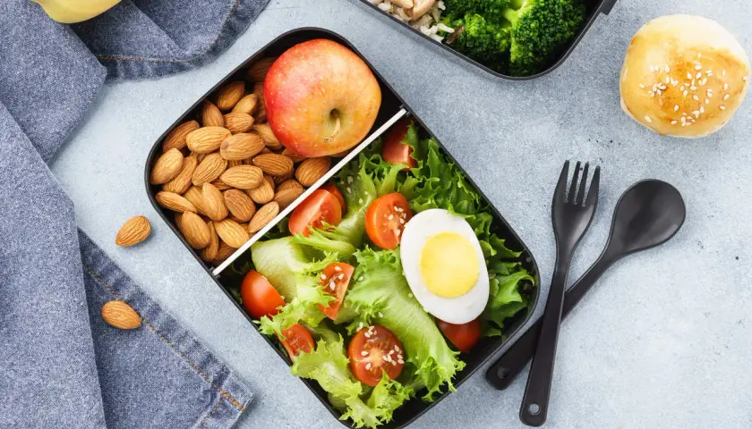 Pudełko na lunch z sałatką, jajkiem, pomidorkami, migdałami i jabłkiem.