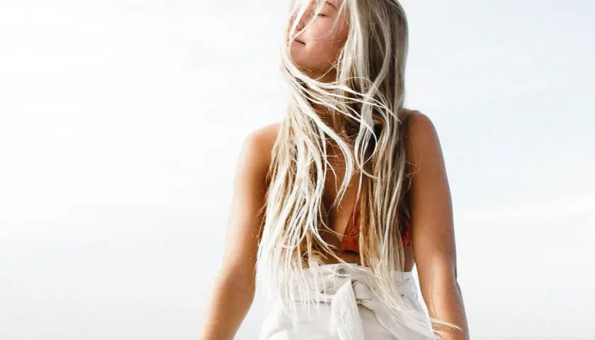 En kvinna med långt, blont hår som blåser i vinden. Hennes hår har en naturlig blondme blekning som ger det en solkysst look.