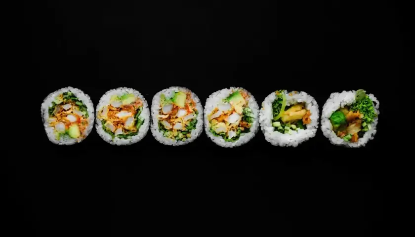 Sześć grubych rolek sushi futomaki z widocznym nadzieniem na czarnym tle.