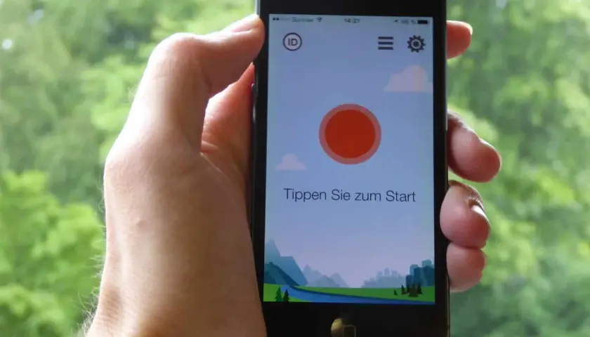 Ein Smartphone wird gehalten, um Vogelstimmen vorspielen zu lassen. Die App zeigt eine Landschaft und den Text "Tippen Sie zum Start".