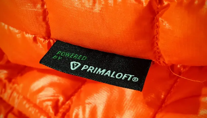 Pomarańczowa, pikowana tkanina z wszywką "Powered by Primaloft®". To materiał izolacyjny, który zapewnia ciepło.
