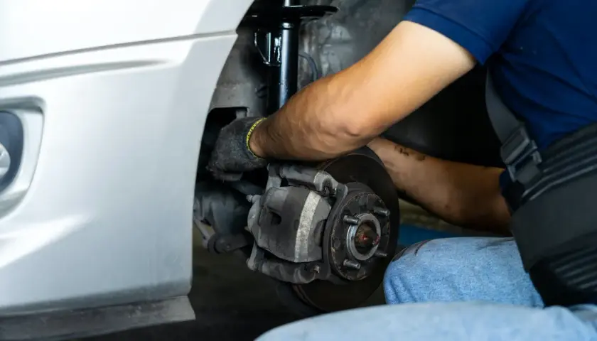 Mecánico trabajando en el sistema de frenos y amortiguadores de un coche. Merece la pena cambiar amortiguadores para una conducción segura.