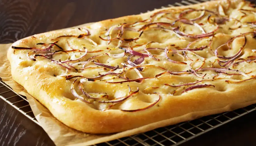 Focaccia dorada con finas rodajas de cebolla balsámica y sal gruesa, recién salida del horno.