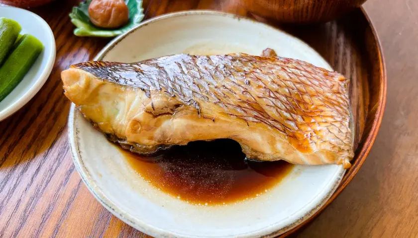 A perfectly cooked piece of karei no nitsuke, its skin crisped and glazed, rests in a savory sauce. Served with pickled plum and okra.