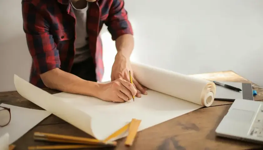 Un uomo disegna su un rotolo di carta, pianificando la posa di piastrelle al metro quadro.