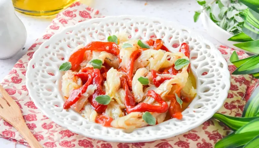 Deliciosa ensalada de bacalao con pimientos rojos asados y hierbas frescas, servida en un plato blanco decorado.